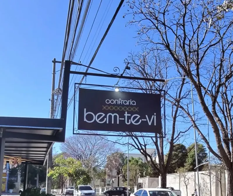 Placa da Confraria Bem Te Vi de dia, céu azul, árvores da avenida